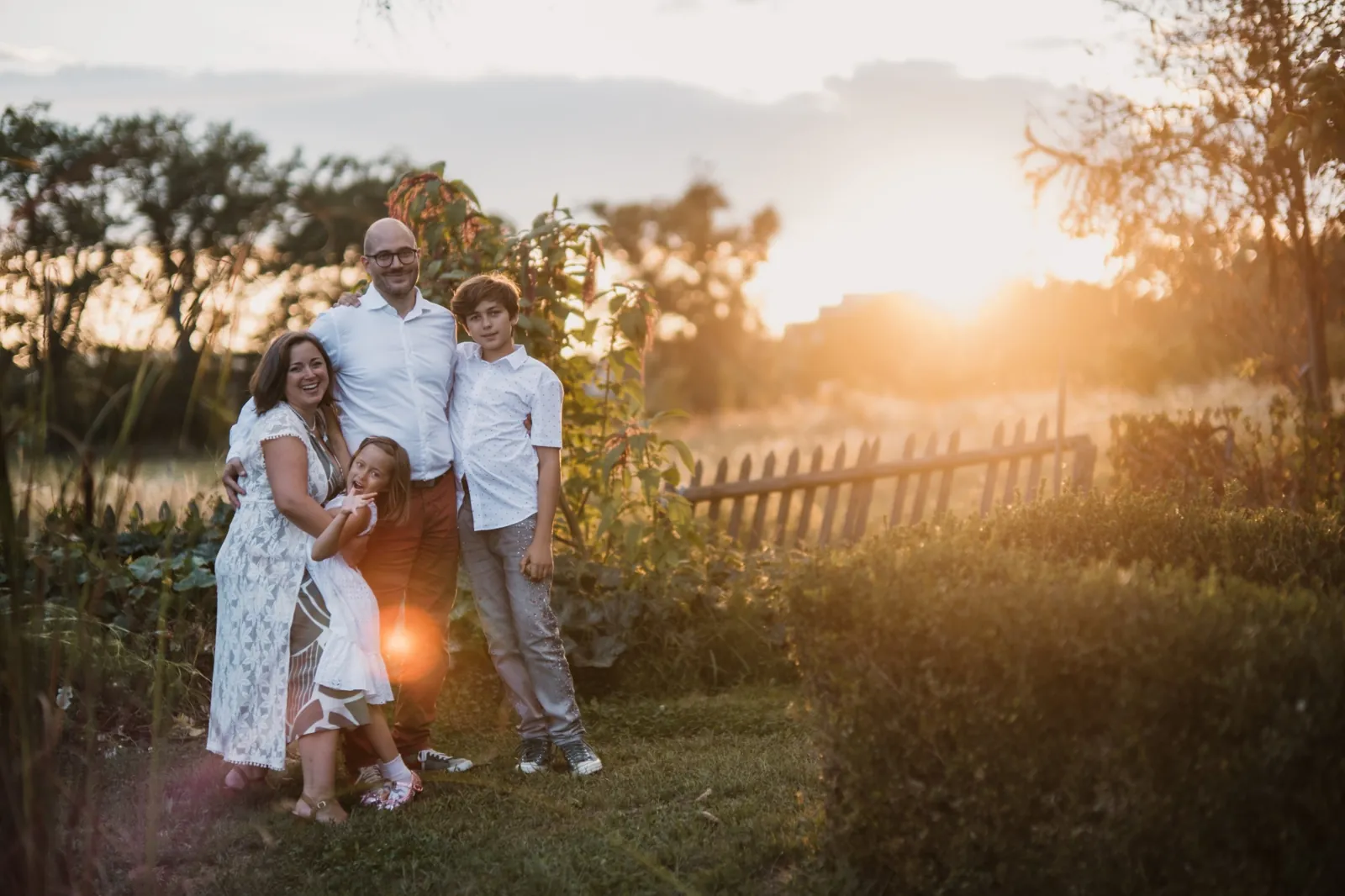 Die Familie steht lachend im Garten im goldenen Gegenlicht des Sonnenuntergangs