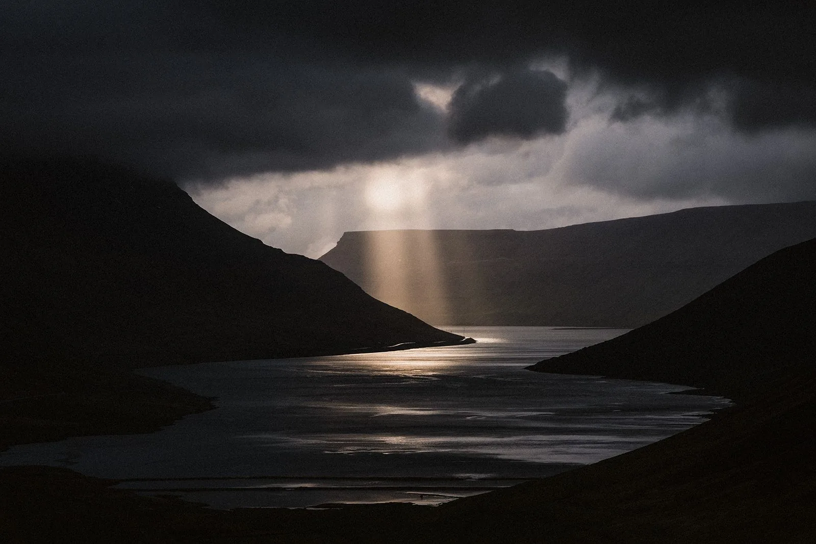 Sonnenstrahlen brechen durch dunkle Wolken und fallen auf einen Fjord in den Westfjorden