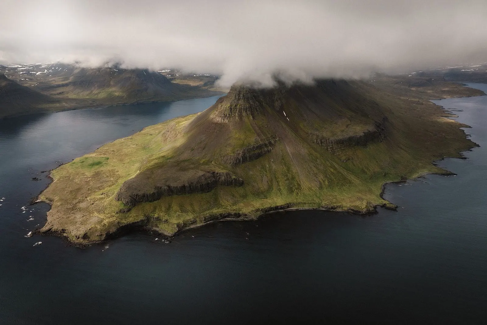 Luftbild einer grünen Halbinsel in den Westfjorden unter tiefen Wolken