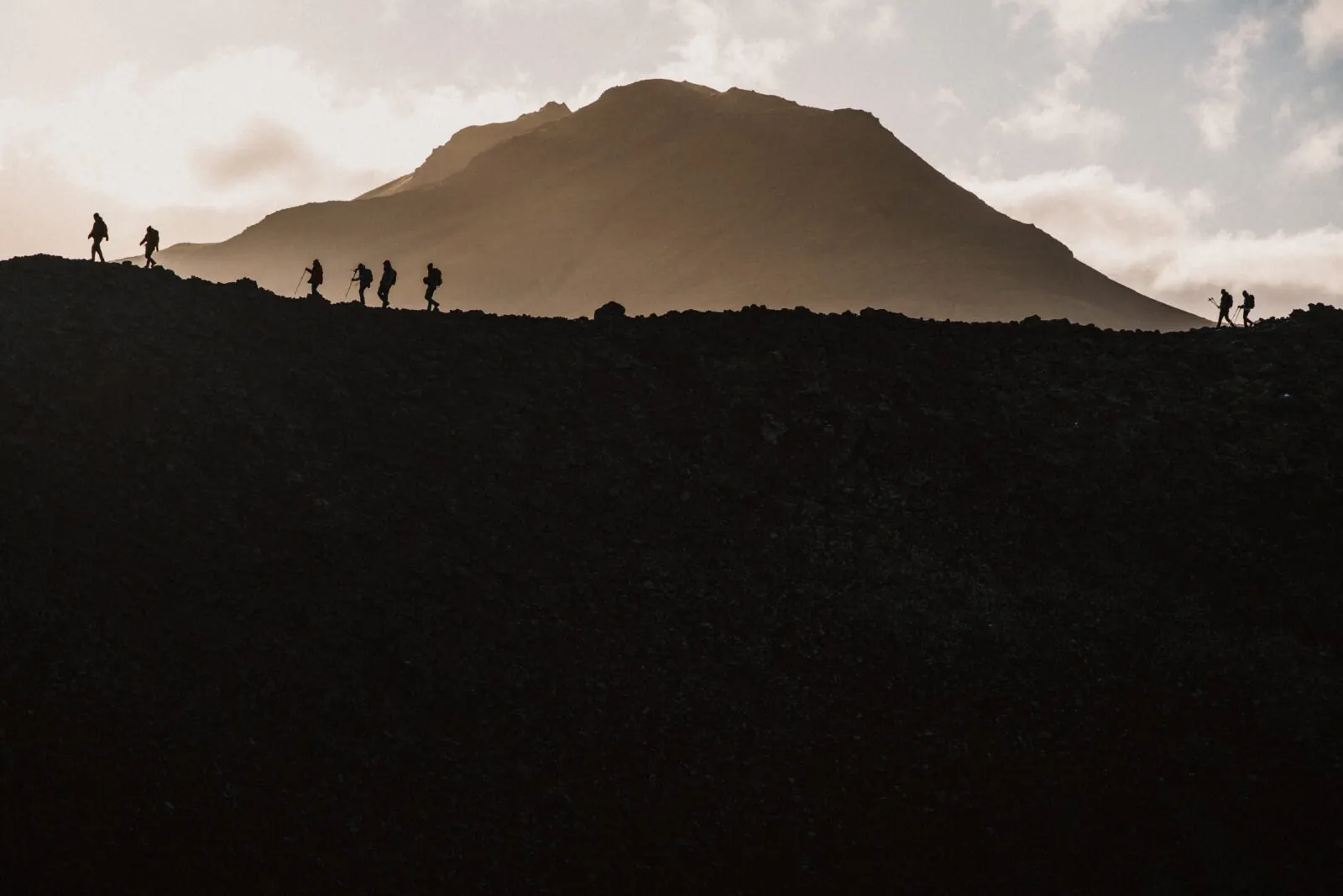 Eine Wandergruppe als Silhouette auf einem Grat vor einem Berg im Abendlicht, Island